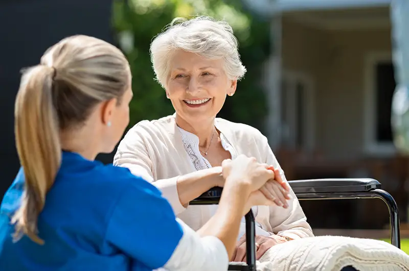 Smiling senior patient sitting on wheelchair with nurse supporting her.