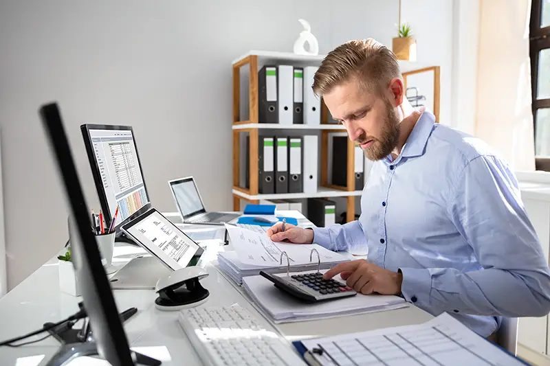 Businessperson Calculating Invoice With Computer On Desk