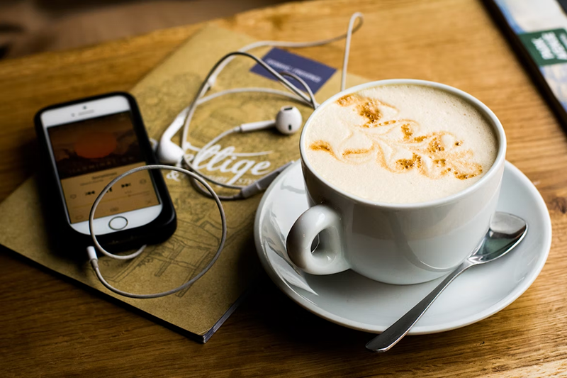 A cup of coffee near smartphone and headset