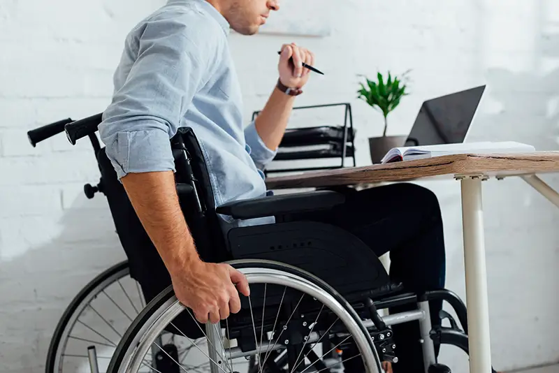 Disabled man sitting on his wheelchair in front of his laptop