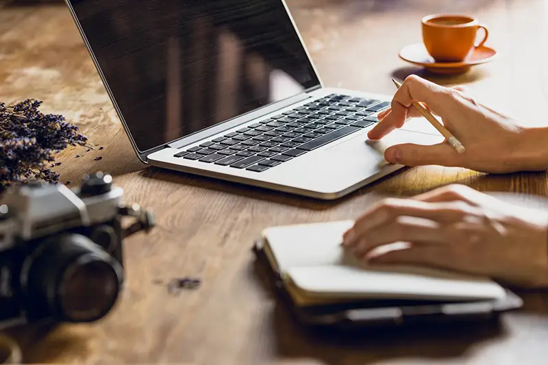 person using laptop and diary at workspace with vintage photo camera