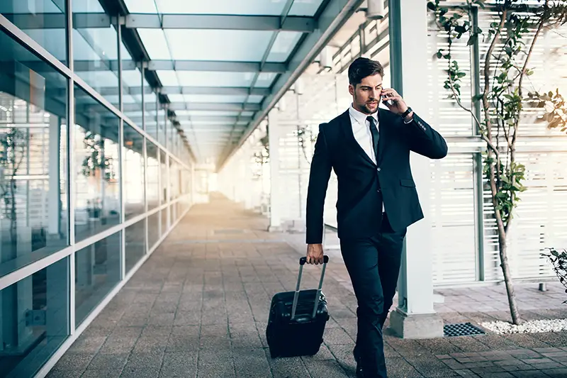 Handsome young man on business trip walking with his luggage and talking on cellphone at airport