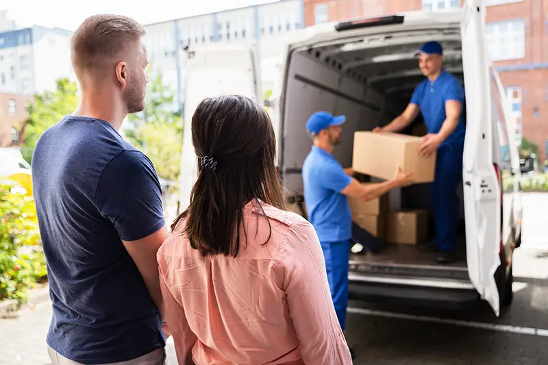 Couple Watching Movers Unload Boxes From Truck