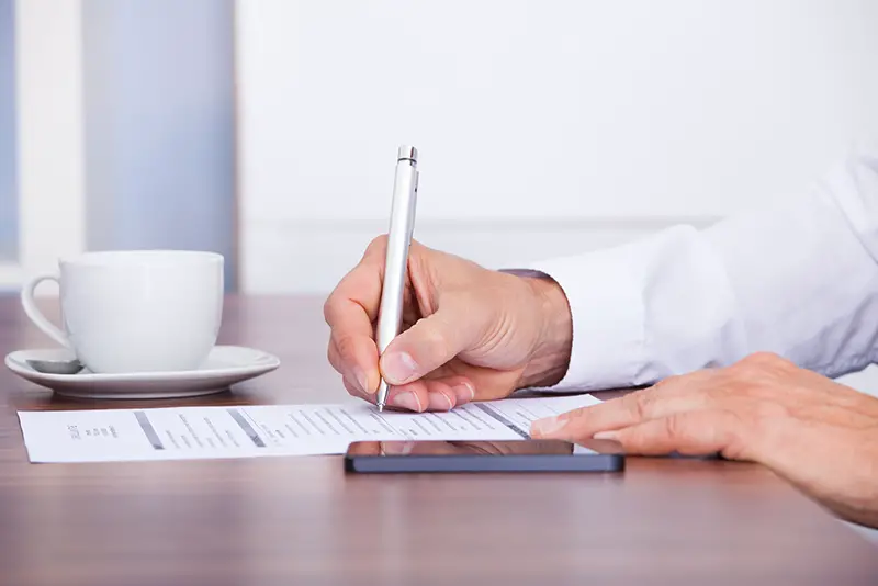 Close-up Of Businessman Writing On Paper With Pen