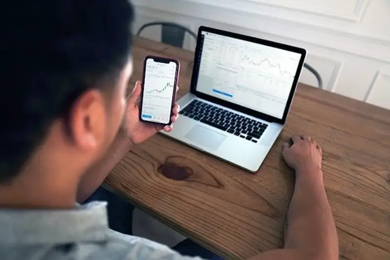 Person using laptop and mobile phone for trading