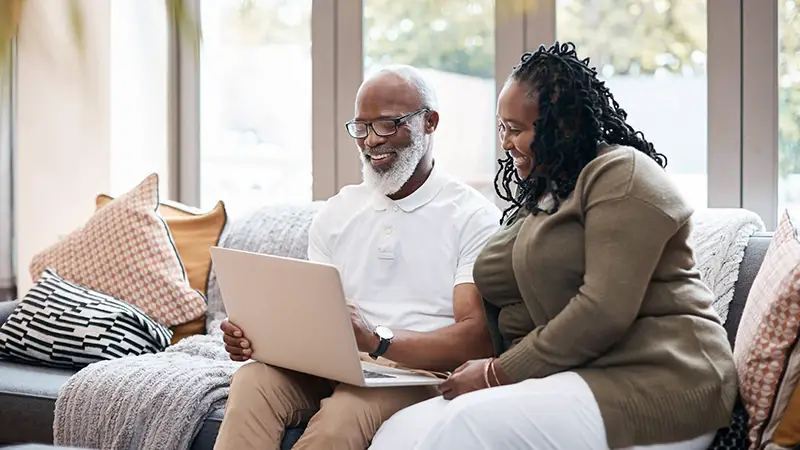 Male senior and a woman using laptop while sitting in the couch