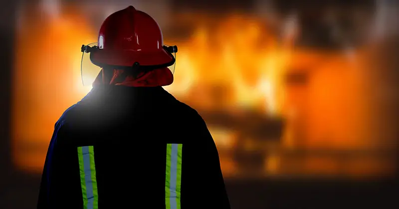 Digital composite of Firefighter in front of burning fire