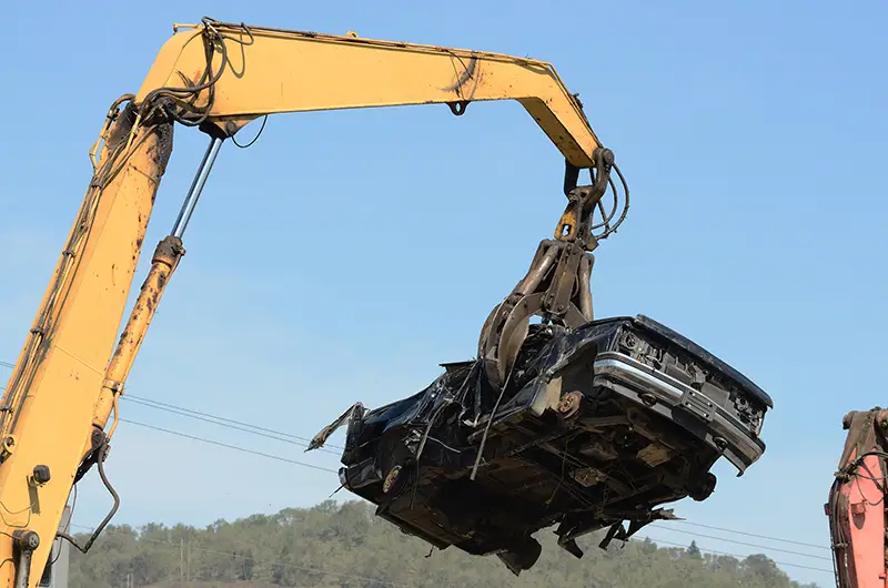 Large excavator with a claw crushing and piling old cars at a metal recycle plant