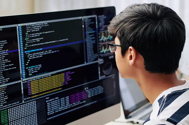 Smart teenage boy in glasses checking programming code on computer screen 