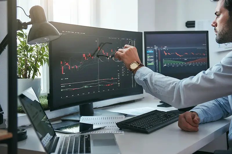 Young trader is pointing at graphs on computer screen and analyzing data 