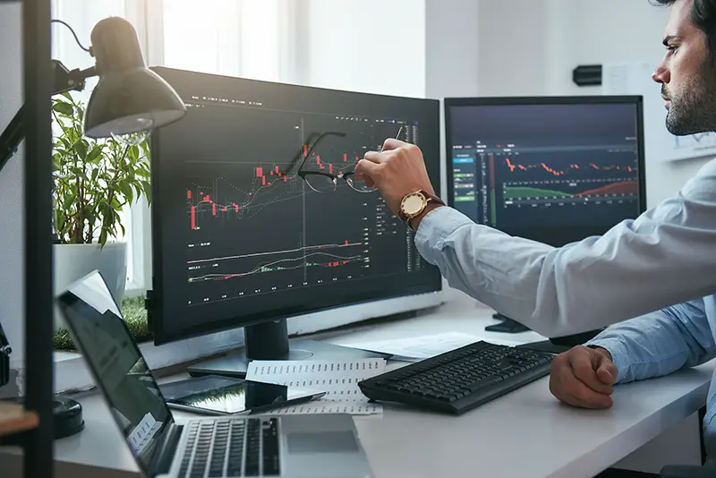 Young trader is pointing at graphs on computer screen and analyzing data