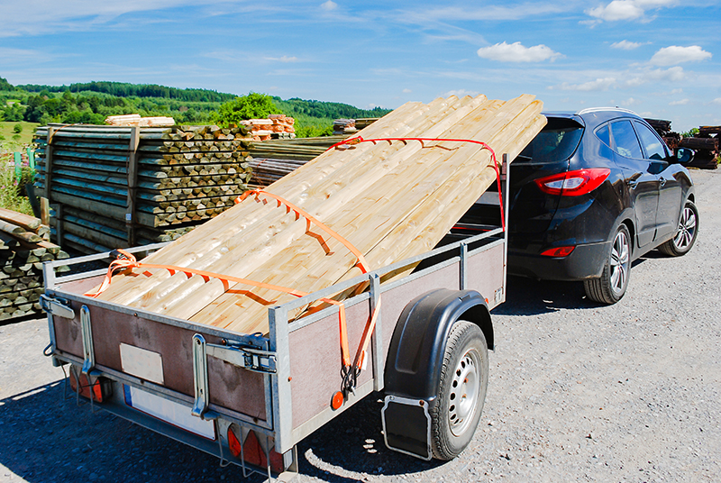 Outdoor stacking the logs on utility trailer for transport 