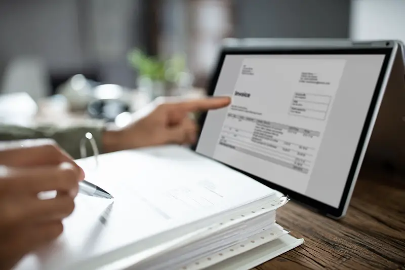 Close-up Of Businessman's Hands Working On Invoice On Laptop At Office