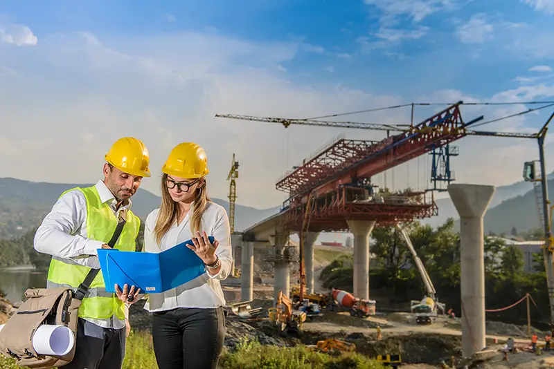 Male and female worker looking at construction plan of the bridge 