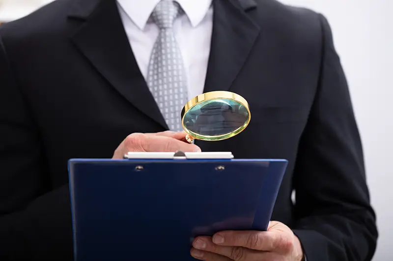 Close-up Of Businessman Analyzing Document Through Magnifying Glass At Workplace