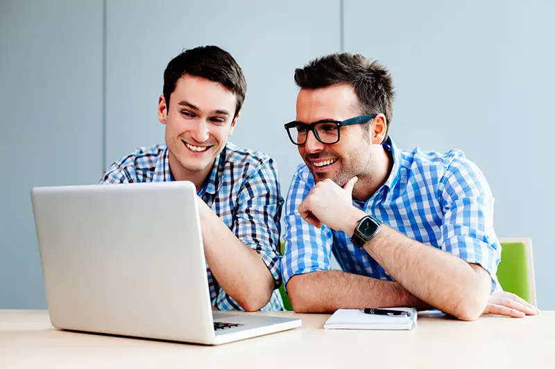 Two smiling webdesigners looking at their project on a laptop