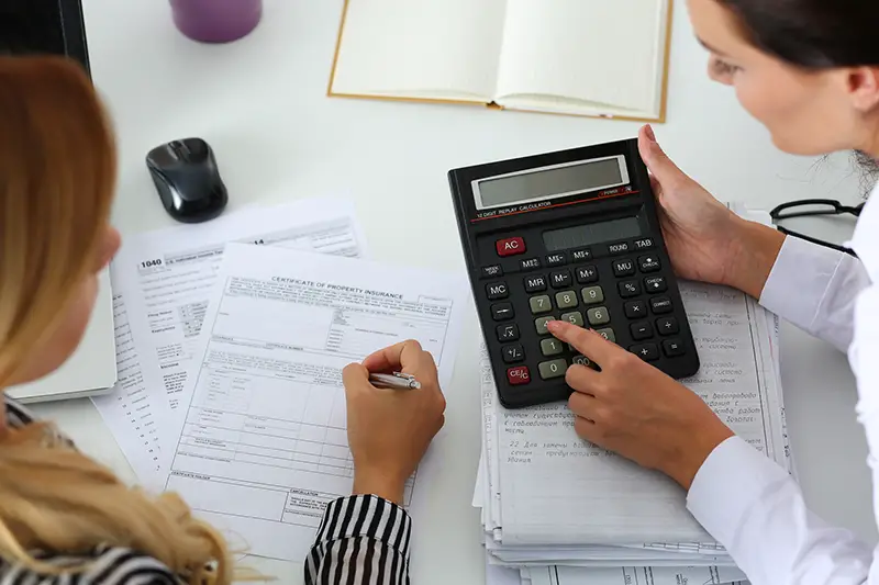 Two female accountants counting on calculator income for tax form completion 