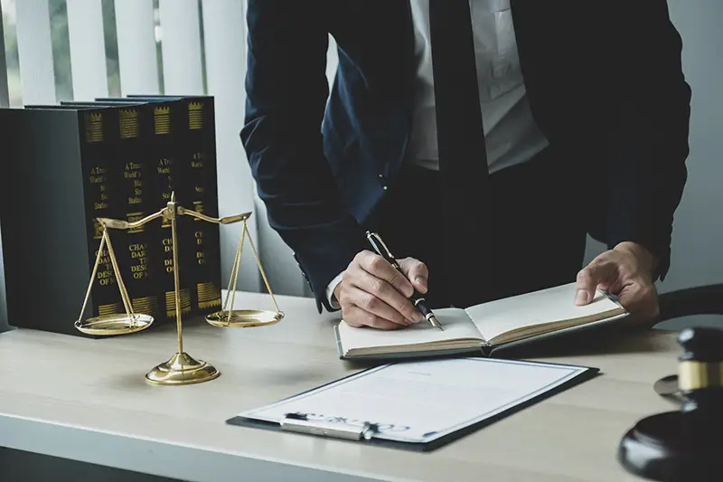 Lawyer hand holding pen and providing legal consult business dispute service at the office with justice scale and gavel hammer.