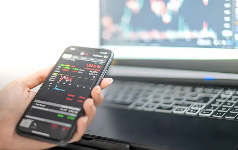 Female trader investor broker analyst holding smartphone in hand analyzing stock market trading charts