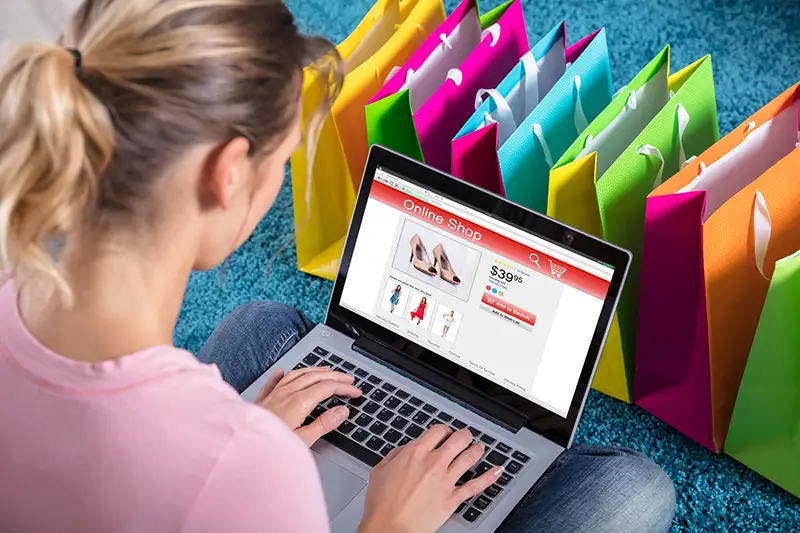 Close-up Of Woman Shopping Online Using Laptop With Colorful Shopping Bags On Carpet