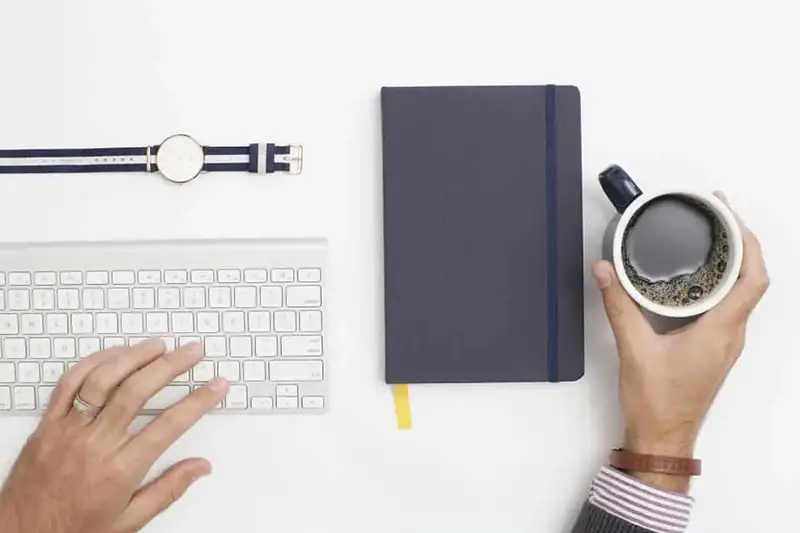 Hand of a person holding a cup of coffee near notebook and keyboard