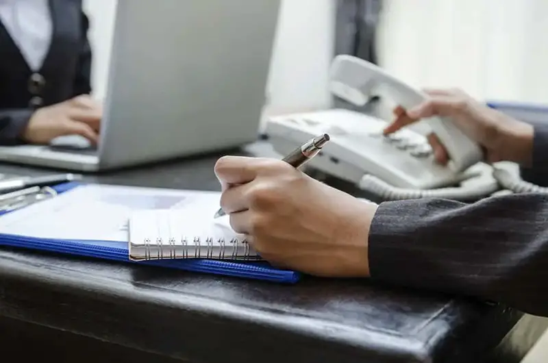 Man taking notes while using white landline phone