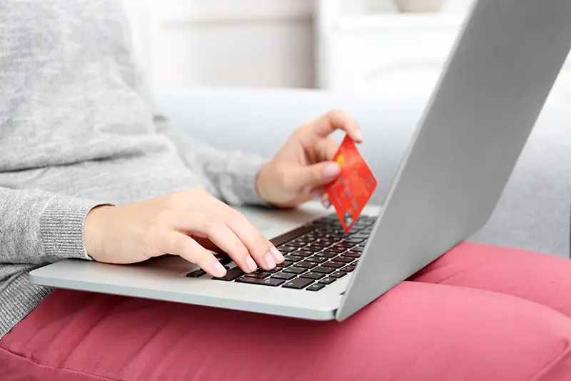 woman with laptop and credit card sitting on sofa, at home