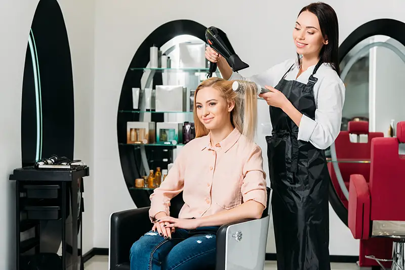 Smiling hairdresser drying customer hair at salon