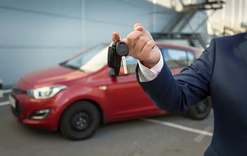 Closeup shot of sales manager holding car keys against new car