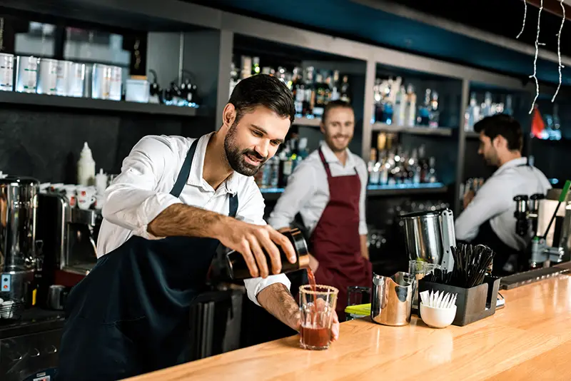 Smiling bartender pouring cocktail in glass at the bar counter