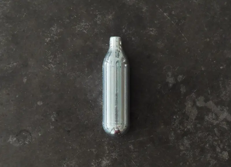 Top view of a nitrous oxide capsule on a concrete surface
