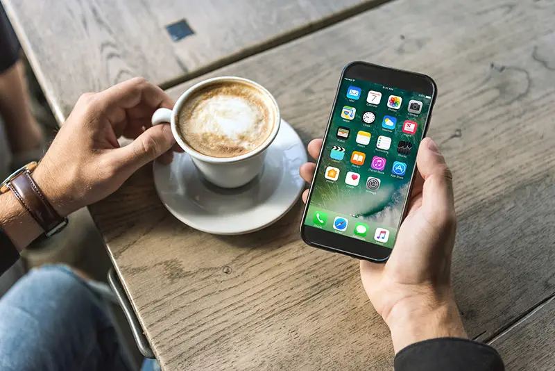 Cropped shot of man with cup of cappuccino using mobile phone apps on the screen