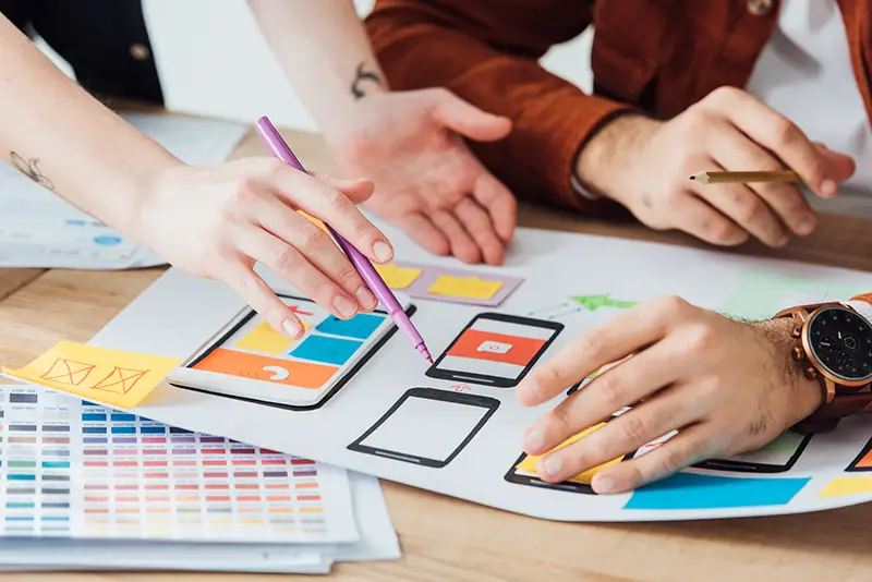 Cropped view of designers planning user experience design of mobile website with frameworks on table isolated on grey