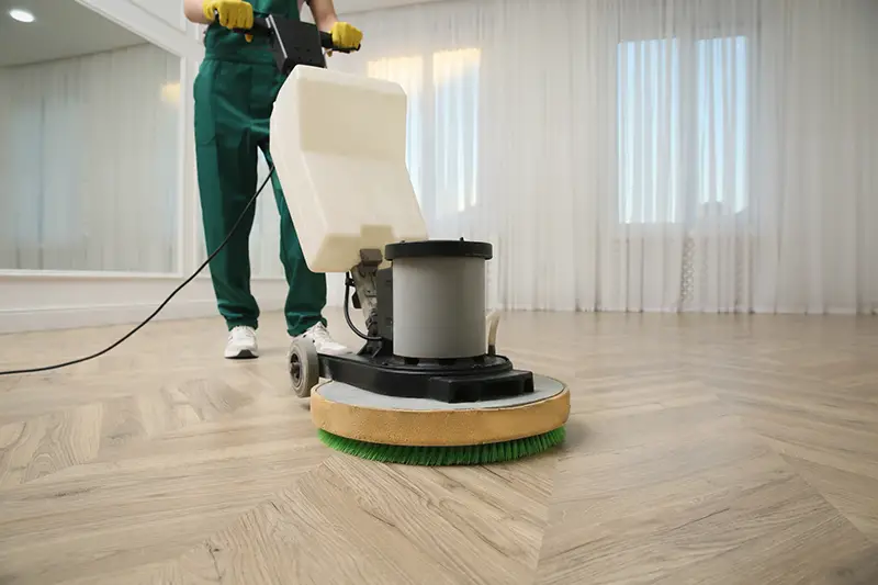 Professional janitor cleaning parquet floor with polishing machine indoors