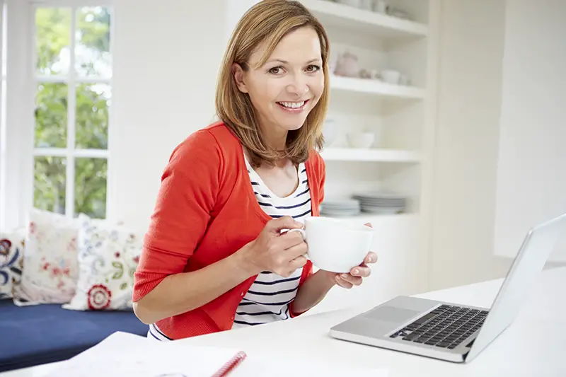 Woman Working From Home Using Laptop In Kitchen