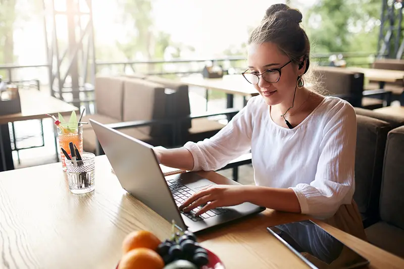 Businesswoman working remotely at cafe with headset and laptop.