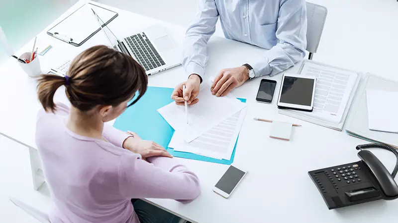 Advisor meeting with a customer in his office, he is explaining a contract document and policy to the woman sitting at his desk