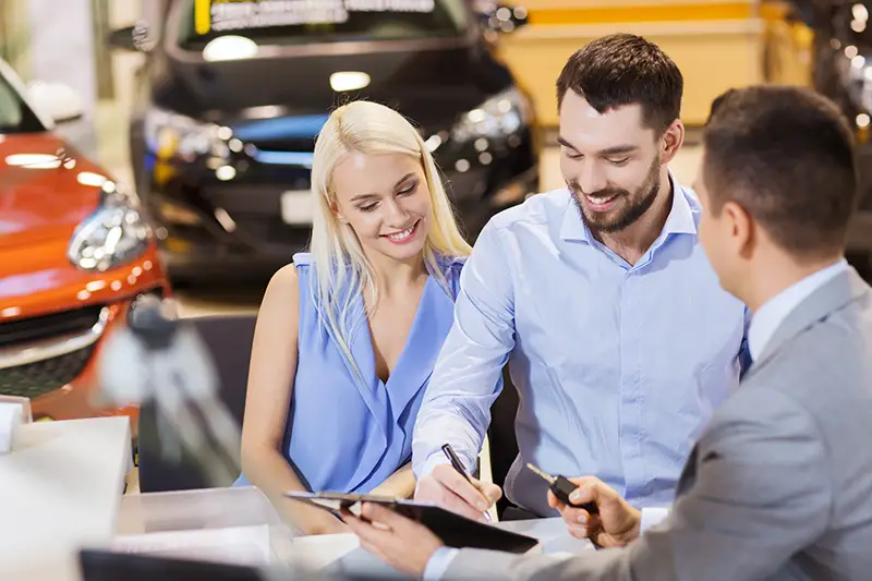 happy couple with dealer buying car in auto show or salon