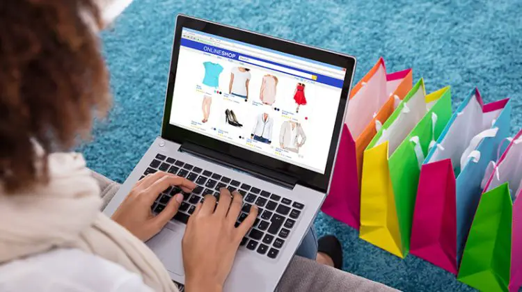 Woman Shopping Online On Laptop With Multi Colored Shopping Bags On Carpet