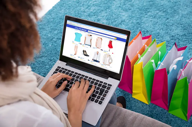 Woman Shopping Online On Laptop With Multi Colored Shopping Bags On Carpet