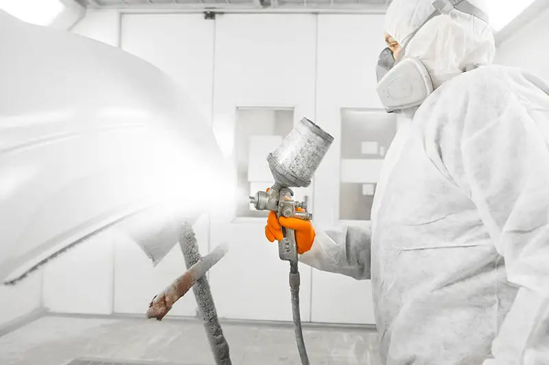 Auto mechanic worker painting a white car with spray gun in a paint chamber