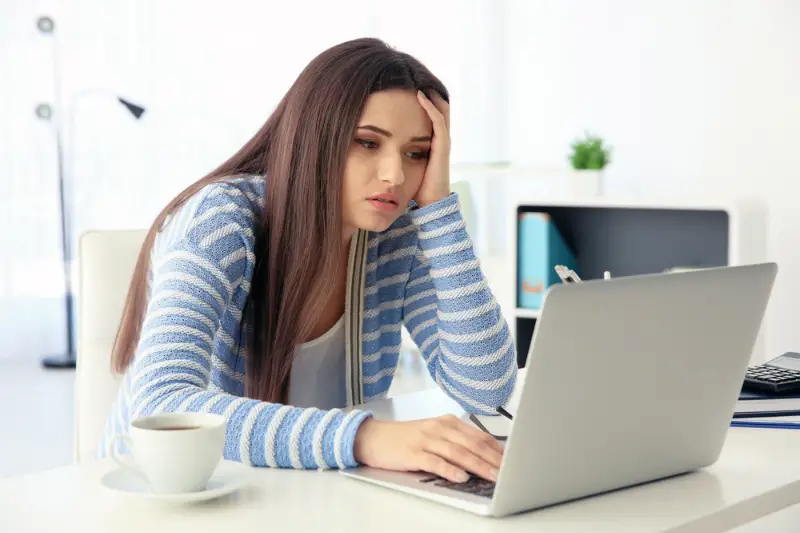 Tired woman sitting at workplace with laptop