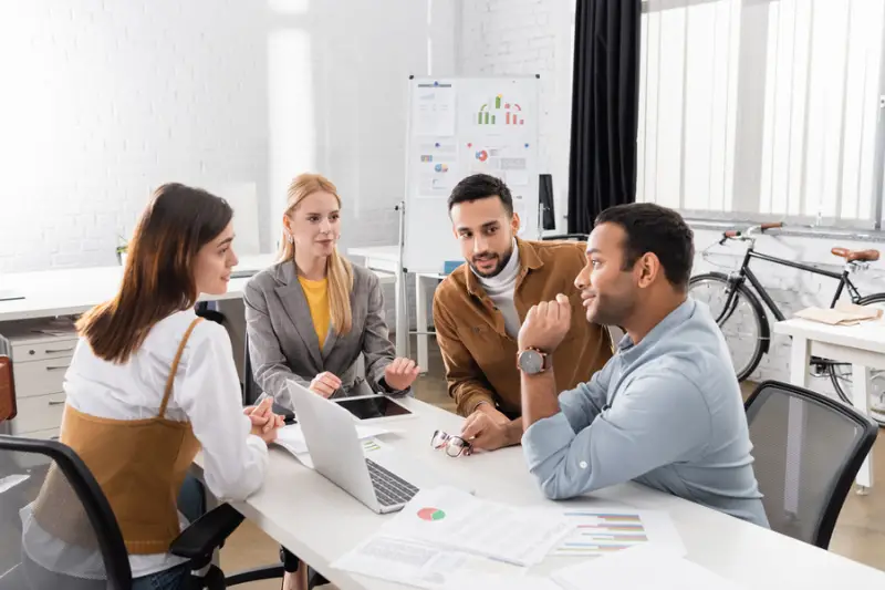 Multicultural businesspeople talking near devices and papers in the office