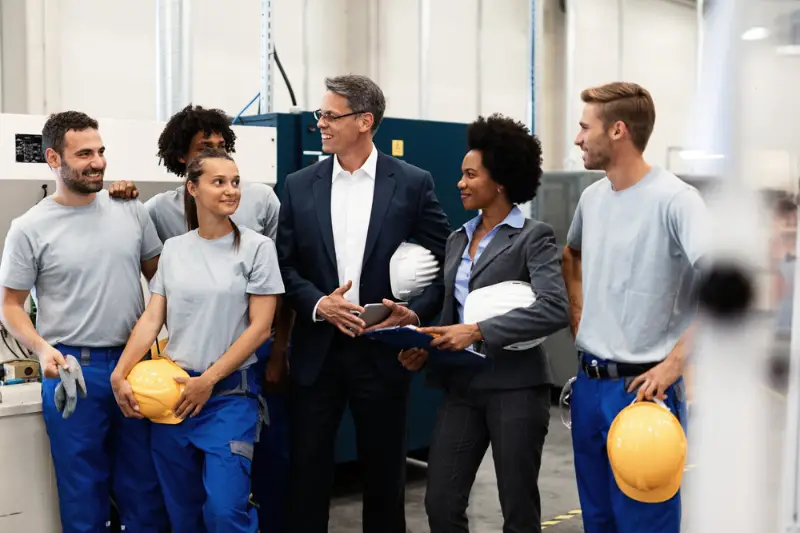 Happy business colleagues communicating with the group of factory workers in the industrial plant