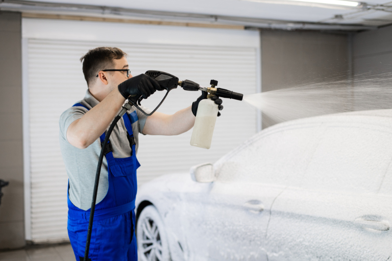 Worker covering automobile with foam at car wash