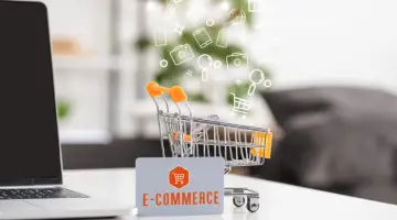 Toy cart beside credit card with e-commerce lettering and laptop on the table