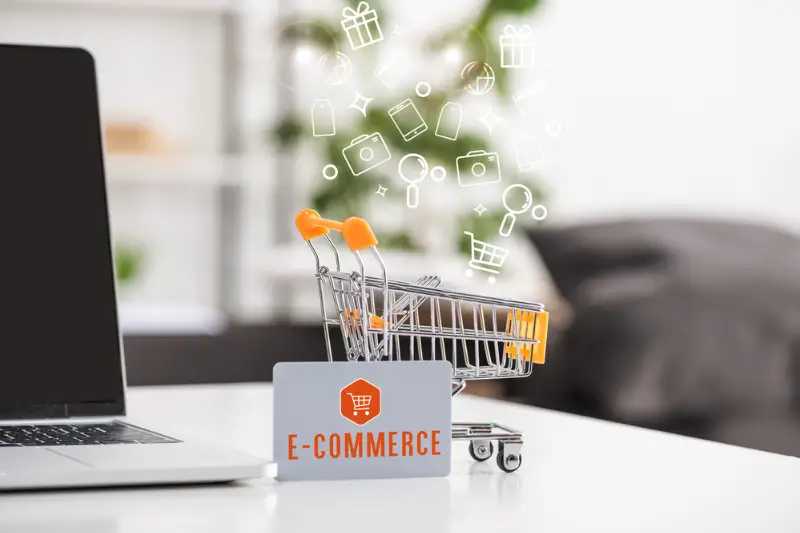 Toy cart beside credit card with e-commerce lettering and laptop on the table