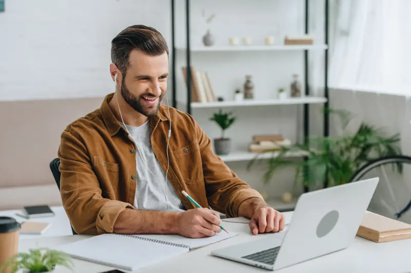 Good-looking man listening music, using laptop while studying online