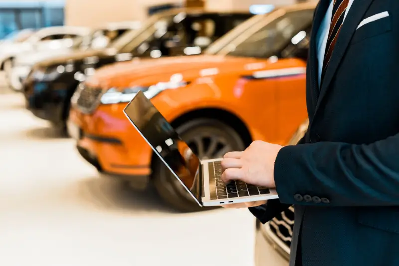 businessman in formal suit using laptop in car dealership