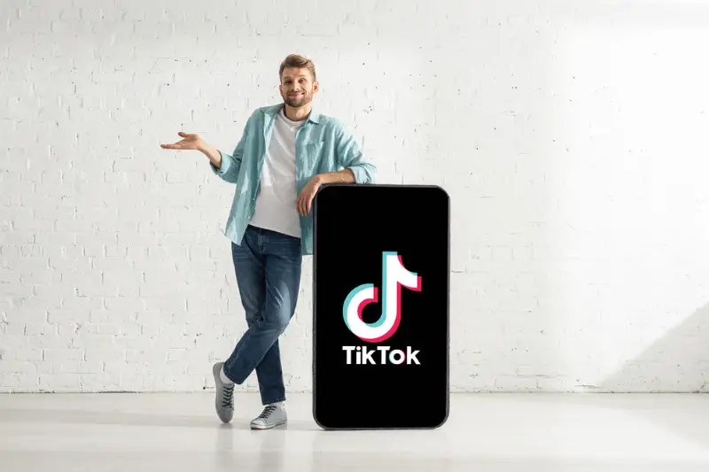 Smiling man standing beside the big Tiktok app